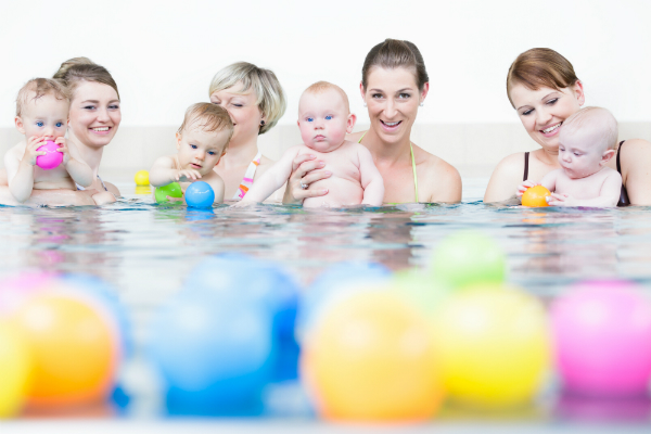 Mamas und Neugeborene spielen beim Babyschwimmen mit Baellen